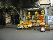 Fruit stall on the edge of the sidewalk, with lights, political poster, and four policemen