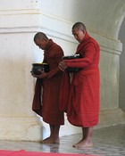 Monks with begging bowls stop to pray in ThatByInNyu as they go about their daily rounds for food.